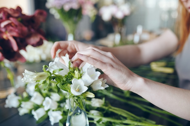 Close de uma mulher irreconhecível ajustando flores brancas em um vaso enquanto faz o buquê na floricultura