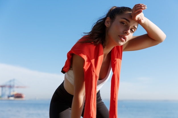 Foto close de uma mulher jovem e atraente fitness fazendo uma pausa durante uma corrida