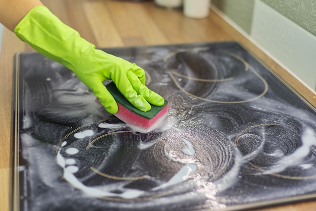 Foto close de uma mulher limpando a superfície de vitrocerâmica de cozinha moderna com esponja e detergente