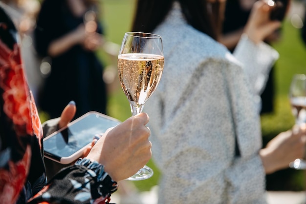 Close de uma mulher segurando uma taça de champanhe e um smartphone em uma festa ao ar livre