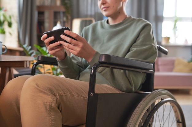 Close de uma mulher sentada em uma cadeira de rodas, digitando no celular, falando online durante seu tempo de lazer