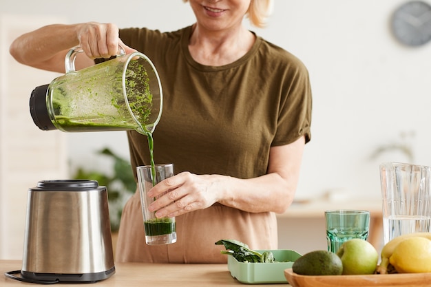 Close de uma mulher servindo suco do liquidificador no copo e bebendo pela manhã