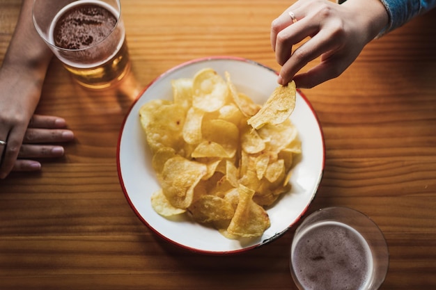 Close de uma mulher tirando uma batata frita do prato para comê-la Ela está em um bar com um amigo