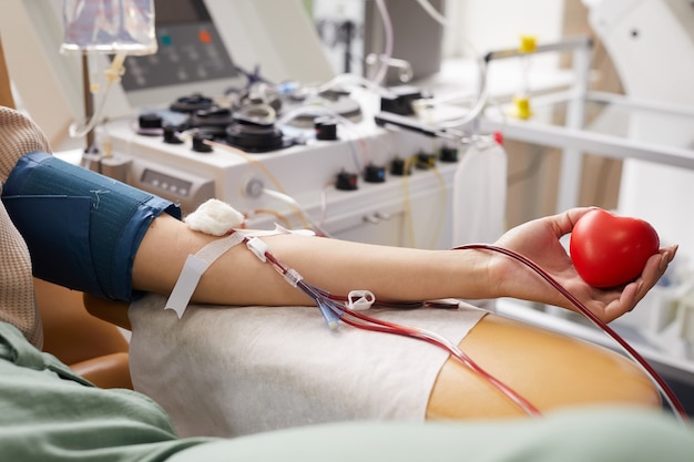 Close de uma paciente com tubos no braço, deitada no sofá enquanto doa sangue no hospital