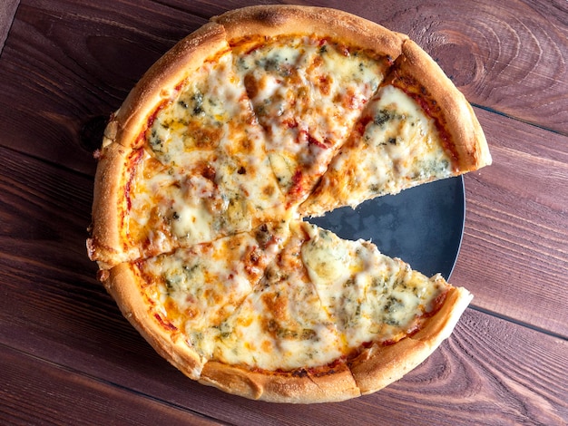 Close de uma pizza italiana pronta com quatro queijos em um fundo de madeira marrom Vista superior plana lay Um prato tradicional da cozinha italiana Cozinha caseira Uma das fatias é comida