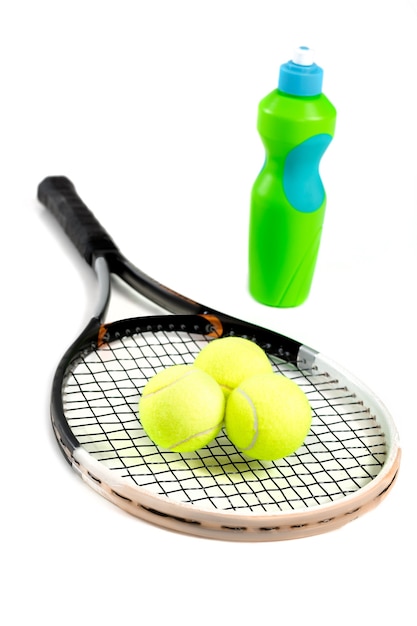 Close de uma raquete de tênis, bolas e uma garrafa de água em branco