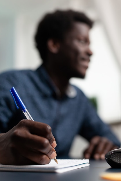 Close do estudante negro escrevendo estratégia financeira no caderno