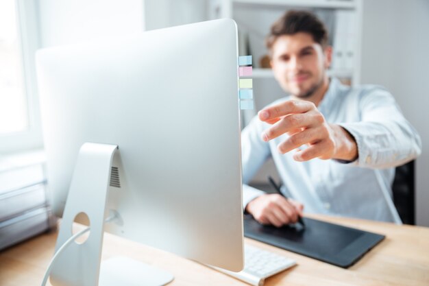 Close do jovem designer colocando adesivos no monitor do computador e usando a mesa gráfica no escritório