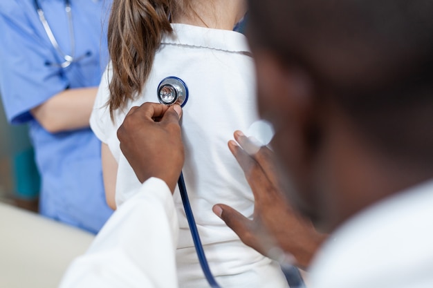 Foto close do médico pediatra afro-americano examinando os pulmões de uma jovem