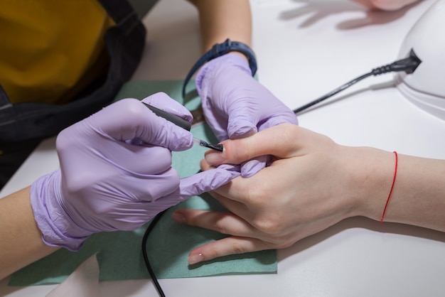 Close do mestre de manicure cobrindo as unhas com o esmalte transparente de unhas femininas em um salão de beleza