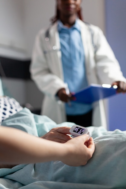 Foto close do oxímetro preso a um paciente idoso doente deitado na cama de hospital, monitorando a hemoglobina