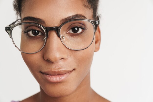 Foto close do retrato de uma mulher afro-americana satisfeita em óculos, olhando para a frente, isolada na parede branca