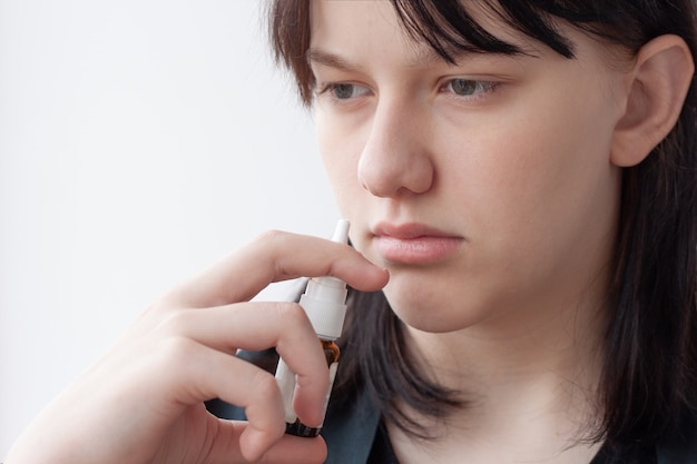 Close do rosto da menina ao lado do nariz um frasco de medicamento para tratamento de congestão nasal nasal