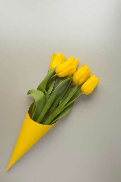 Close em tulipas amarelas em um cone amarelo de papel na superfície cinza