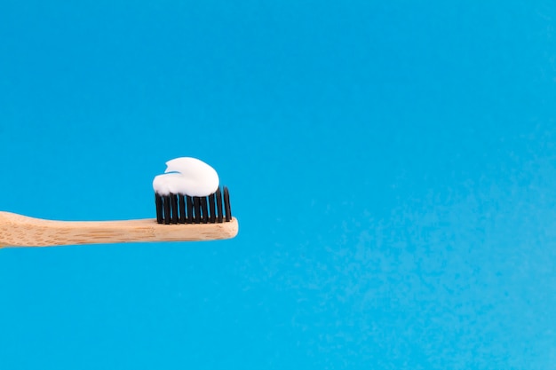 Close na escova de dentes de bambu com pasta branca no fundo azul