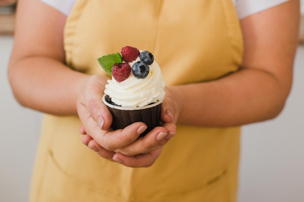 Close nas mãos de uma chef confeiteira em um vestido branco com bolinho ou um bolinho decorado com frutas silvestres