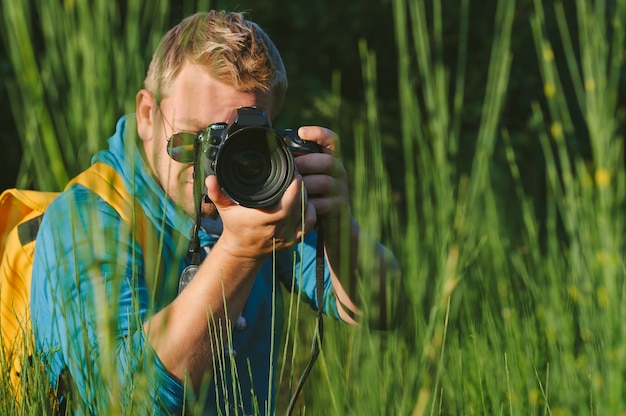 Close, o fotógrafo segura uma câmera fotográfica profissional nas mãos. No contexto da bela natureza verde.