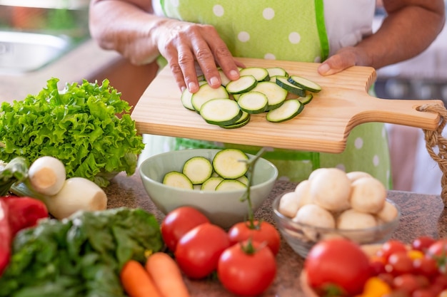 Close up auf weibliche Hände halten ein Schneidebrett mit in Scheiben geschnittenen Zucchini Frisches rohes Gemüse auf dem Tisch