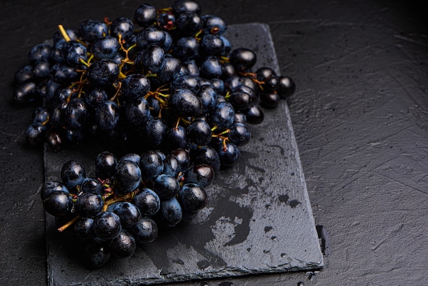 Close-up, bagas de cacho escuro de uva com pouca luz isoladas no fundo preto, gotas de água