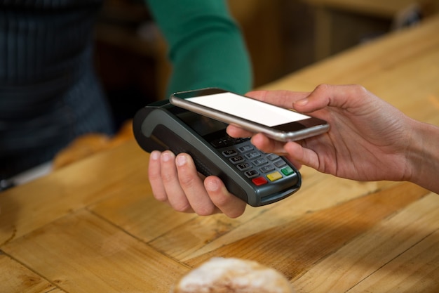 Close-up de barista aceptando pagos a través de teléfonos inteligentes.