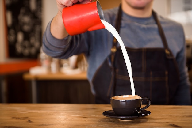 Close-up barista derramando muito leite na xícara de café, fazendo latte art.