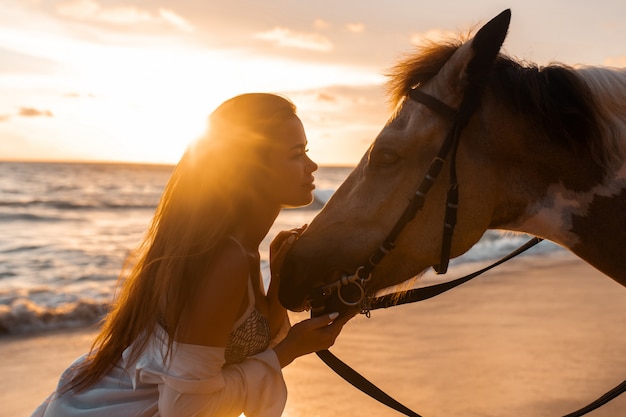 Close-up: beleza morena jovem se divertindo com o cavalo na praia. Pôr do sol