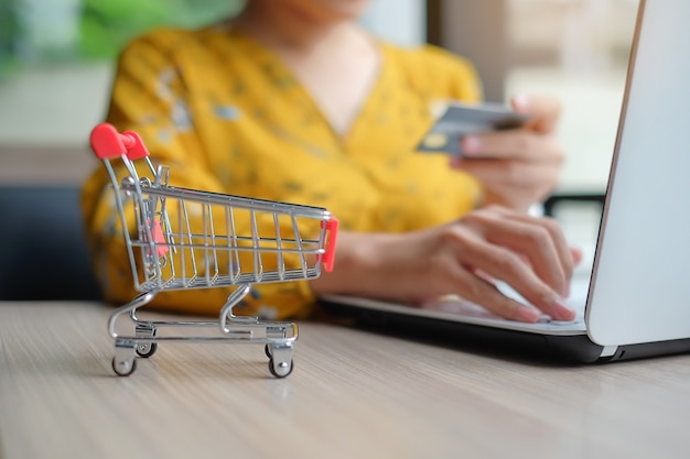 Foto close-up carrinho de compras, mulher asiática segurando o cartão de crédito e usando o laptop para on-line