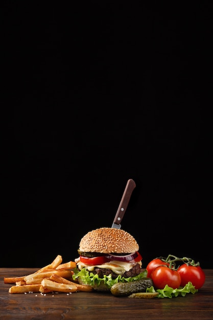 Close-up caseiro de hambúrguer com carne, tomate, alface, queijo, cebola e batatas fritas na mesa de madeira.