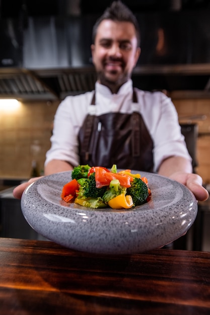 Foto close-up de chef de restaurante dando plato de ensalada en plato redondo encima del mostrador