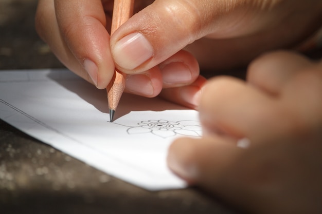 Close-up childs mão desenha uma flor com um lápis em uma folha branca de papel, foco seletivo