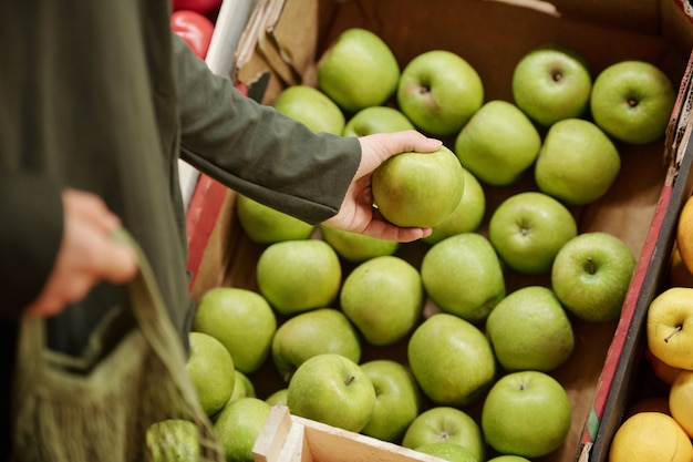 Close-up de cliente irreconocible de pie en el mostrador y elegir manzanas verdes en caja