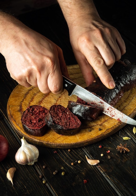 Foto close-up cozinha mãos com uma faca cortar salsicha de sangue em uma tábua de corte de cozinha cozinhar um prato nacional com especiarias em casa na cozinha