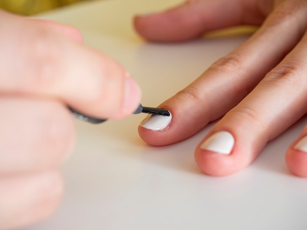 Close-up da aplicação de esmalte branco com um pincel. Manicure em casa. Manicure de baixa qualidade