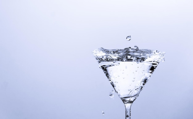 Foto close-up da gota de água caindo em um copo no fundo branco.