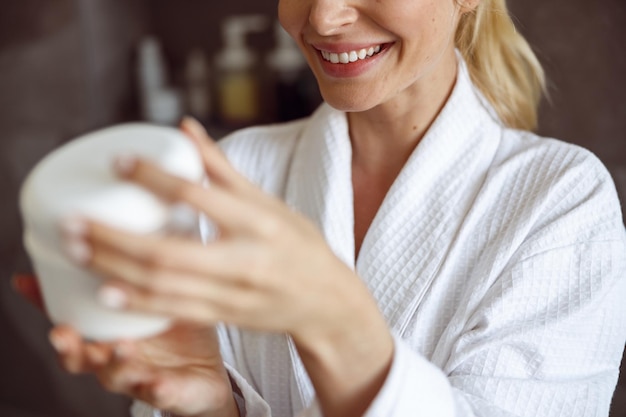 Close-up da jovem mulher caucasiana feliz sorrindo e segurando o creme facial antienvelhecimento