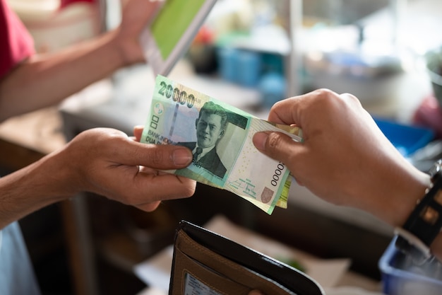 Close-up da mão de um comprador asiático pagando em rúpias para um vendedor de barraca de comida após comer em uma barraca de comida