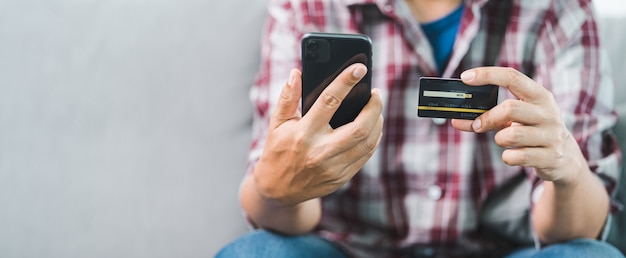 Close-up da mão de um empresário segurando o cartão de crédito e usando o laptop em casa. Homem de negócios ou empreendedor trabalhando, compras online, e-commerce, internet banking, trabalhando em casa conceito