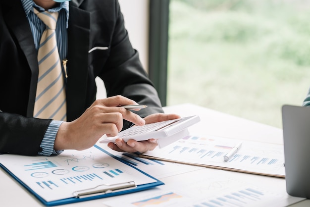 Close-up da mão de um empresário segurando uma calculadora com gráfico de documentos colocado na mesa do escritório.