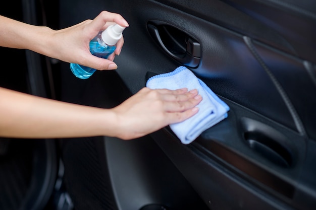 Close-up da mão de uma mulher está limpando o carro com spray de álcool