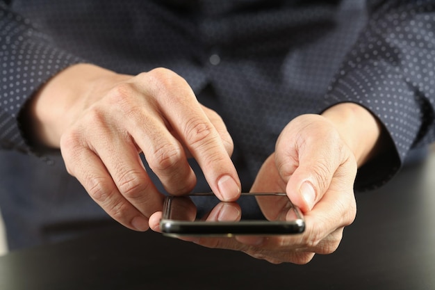 Close-up da mão do empresário trabalhando com telefone celular no escritório moderno