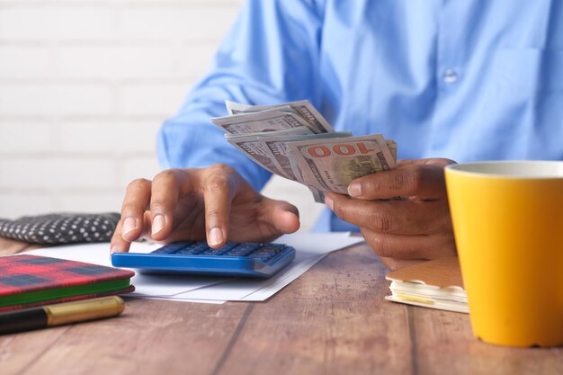 Foto close up da mão do homem usando calculadora e segurando-nos dólar