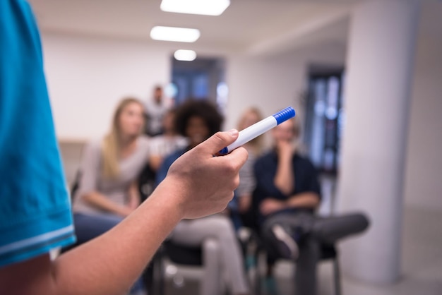 close-up da mão do professor com marcador enquanto ensinava na sala de aula da escola para estudantes multiétnicos