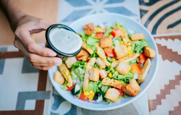 Foto close-up da mão preparando uma salada de legumes conceito de alimentação saudável e estilo de vida mão colocando molho em uma salada caesar
