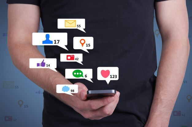 Close-up da mão segurando o telefone móvel com ícones criativos de mídia social em fundo abstrato como tecnologia de rede e conceito de comunicação