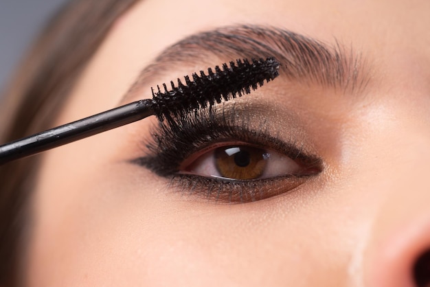 Close up da maquiagem dos olhos. Aplicando maskara em exuberantes Mulher jovem se maquiando com pincel. Mulher de rosto de olhos.