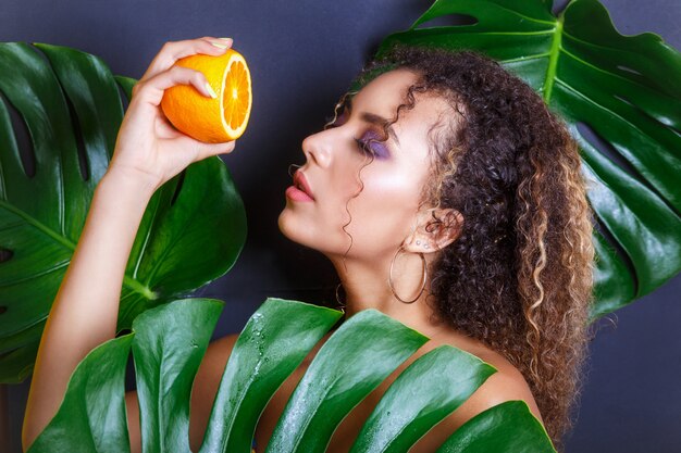 Close-up da menina bonita posando na floresta tropical. Retrato de uma linda mulher afro-americana com frutas tropicais