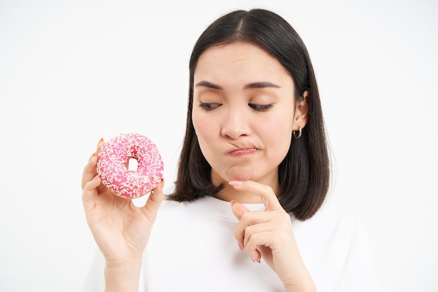 Close-up da menina pensa em frear sua dieta olhando para o tentador fundo branco de rosquinha vitrificada