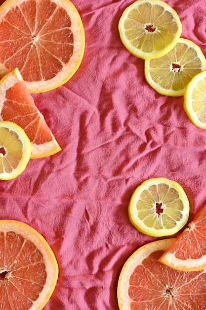 Close-up da moldura de toranja e limão, com fundo de tecido coral, rosa e vermelho, com espaço de cópia