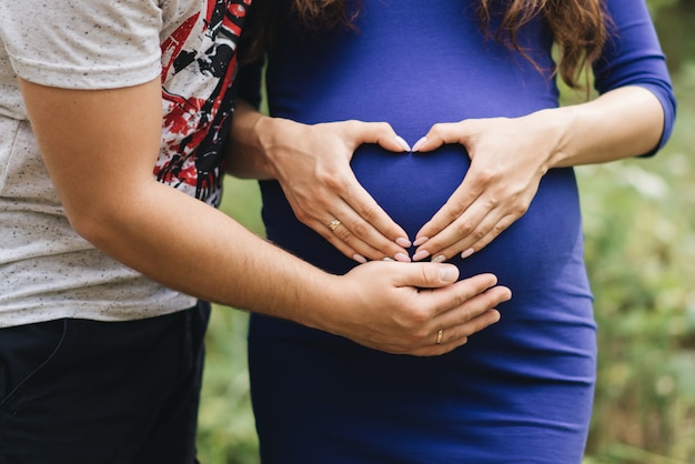 Close-up da mulher grávida irreconhecível com as mãos sobre a barriga ao lado do marido