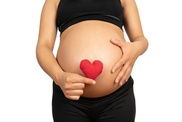 Close-up da mulher grávida segurando o cartaz do coração na barriga contra um fundo branco. Gravidez, conceito de maternidade.